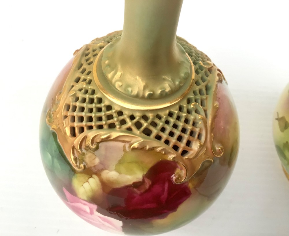 A pair of porcelain vases featuring narrow gilt necks, bulbous bodies hand-painted with pink and crimson roses, and pierced gilt lattice details at the shoulder. View V