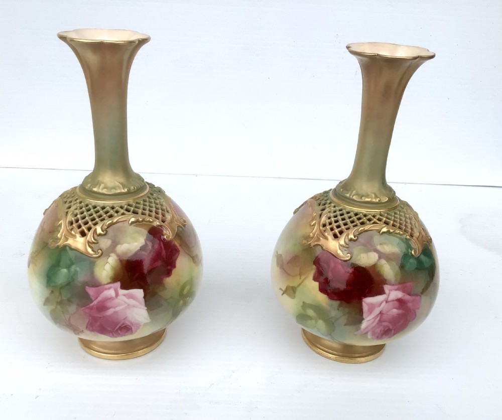 A pair of porcelain vases featuring narrow gilt necks, bulbous bodies hand-painted with pink and crimson roses, and pierced gilt lattice details at the shoulder. View X