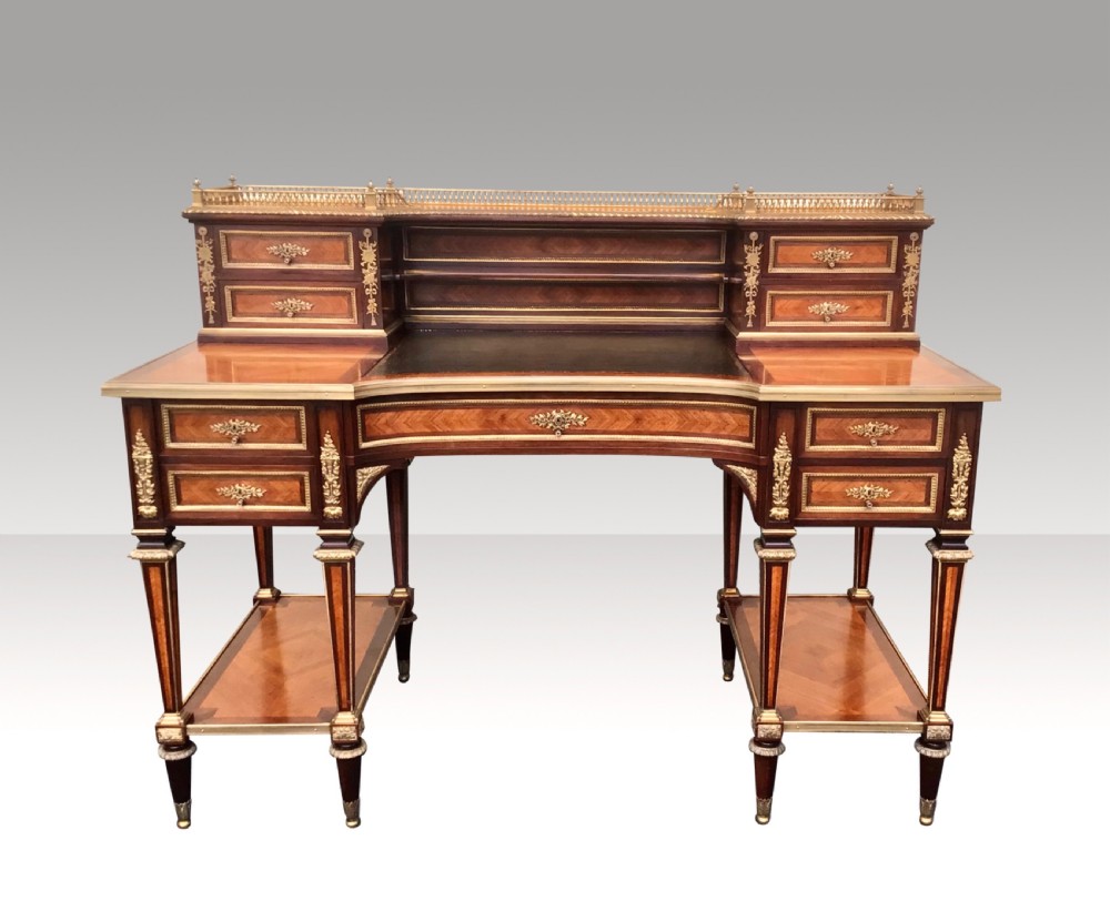 An antique French kingwood writing desk featuring a raised superstructure with small drawers, gilded brass gallery rail, leather insert, and lower side tiers supported by turned legs.