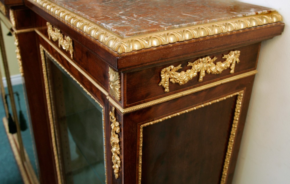 A large dark mahogany breakfront display cabinet featuring four glazed doors, glass interior shelves, and gold ormolu mounts along the frieze and side posts. View II
