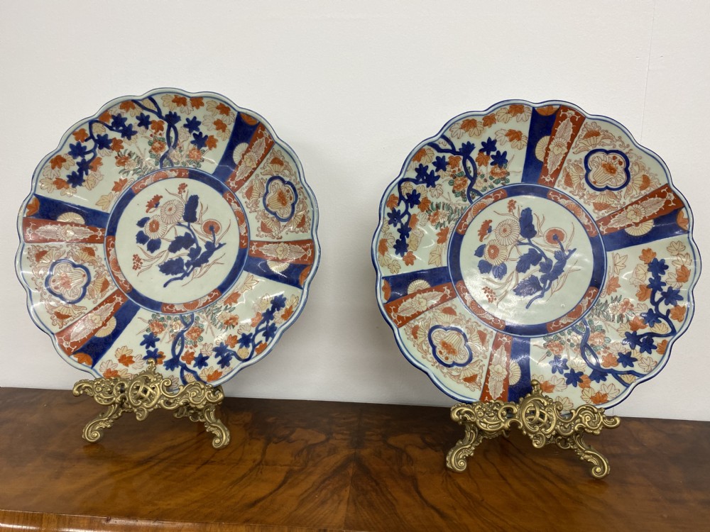 A pair of large Japanese Imari porcelain chargers featuring scalloped rims and hand-painted floral motifs in cobalt blue and iron red.