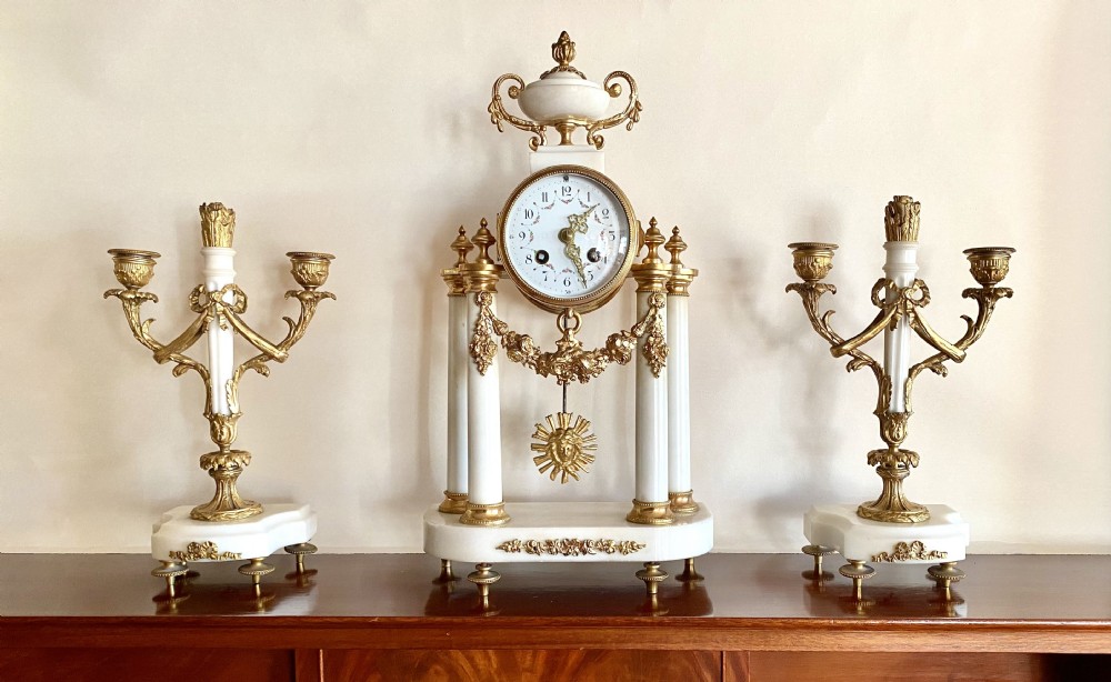 A French Neoclassical three-piece clock garniture crafted from white marble and gilt ormolu, featuring a portico-style pendulum clock flanked by two matching twin-light candelabra. View IV