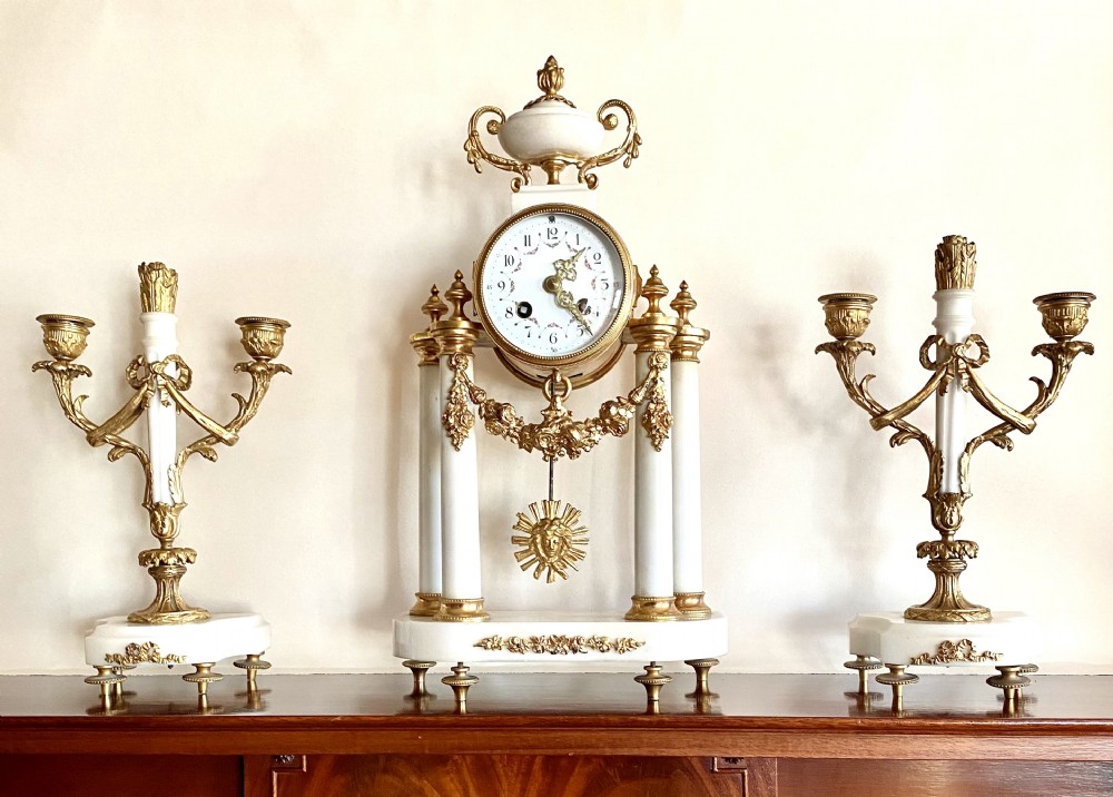 A French Neoclassical three-piece clock garniture crafted from white marble and gilt ormolu, featuring a portico-style pendulum clock flanked by two matching twin-light candelabra. View II