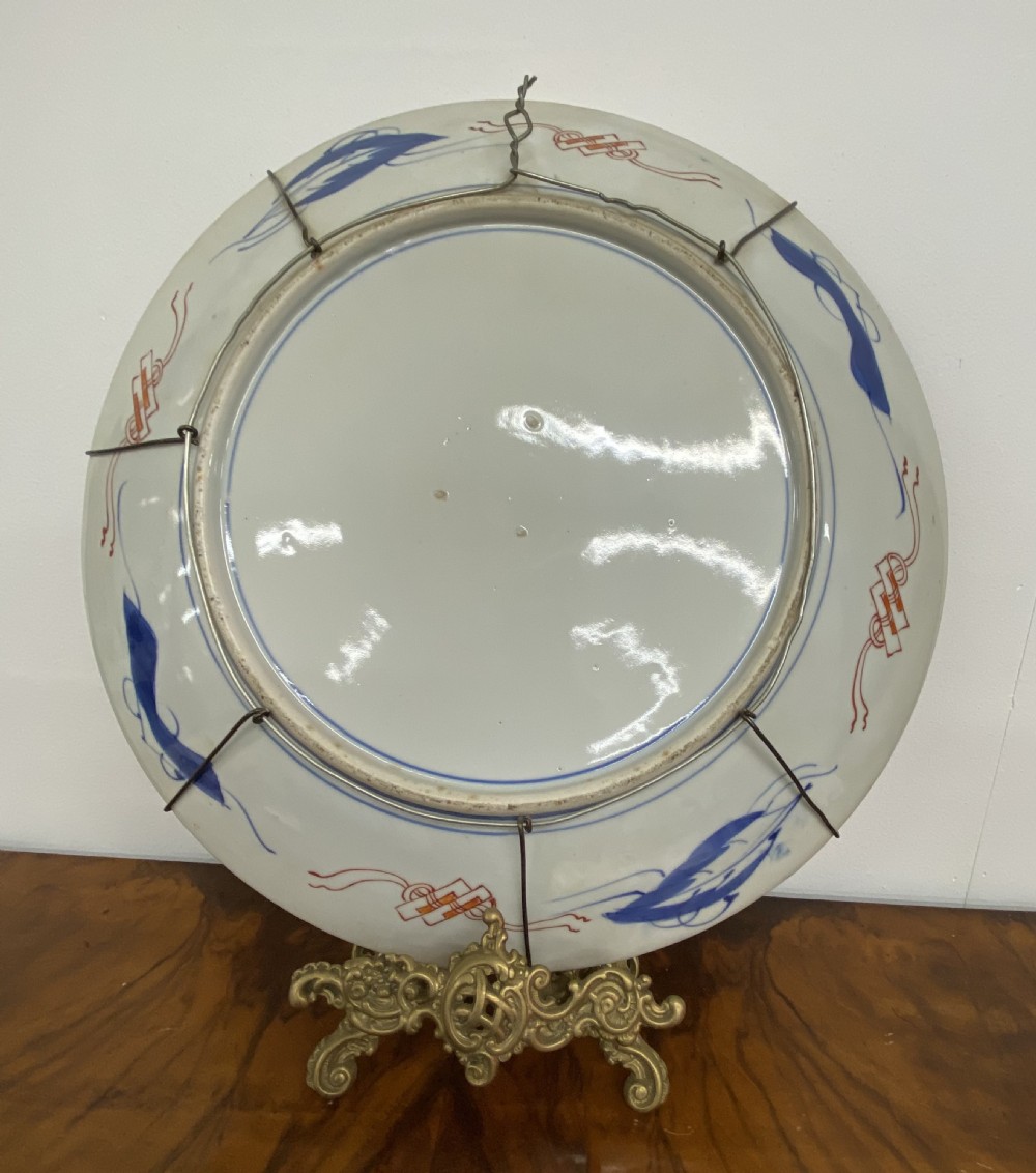 A circular antique Japanese Imari porcelain charger plate decorated with blue, orange, green, and gold panelled designs featuring figures and botanical motifs. View II