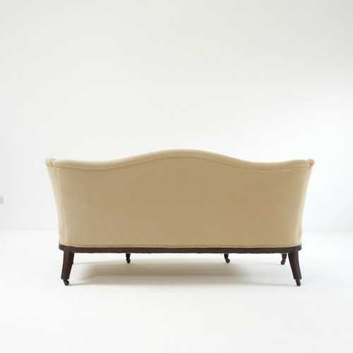 fig 1. A 19th-century serpentine back sofa upholstered in cream fabric featuring a carved mahogany frame with fluted legs and brass castors.