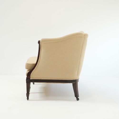 fig 2. A 19th-century serpentine back sofa upholstered in cream fabric featuring a carved mahogany frame with fluted legs and brass castors.