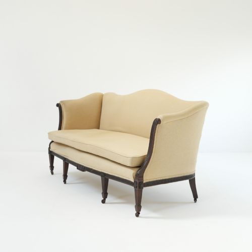fig 3. A 19th-century serpentine back sofa upholstered in cream fabric featuring a carved mahogany frame with fluted legs and brass castors.