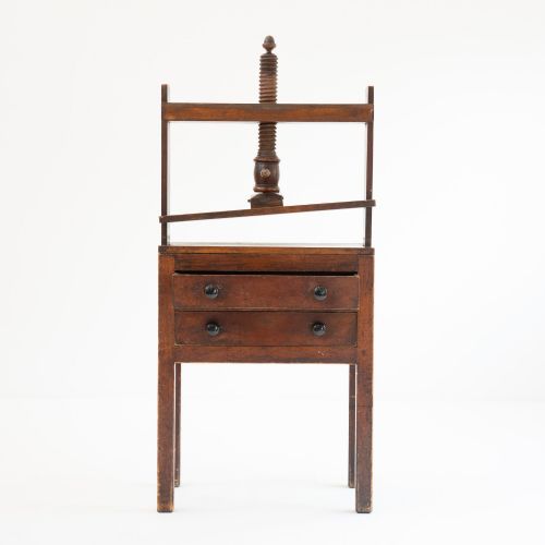fig 2. A Victorian mahogany and pine linen press featuring a central wooden screw mechanism over two small drawers with turned black knobs and four square legs.