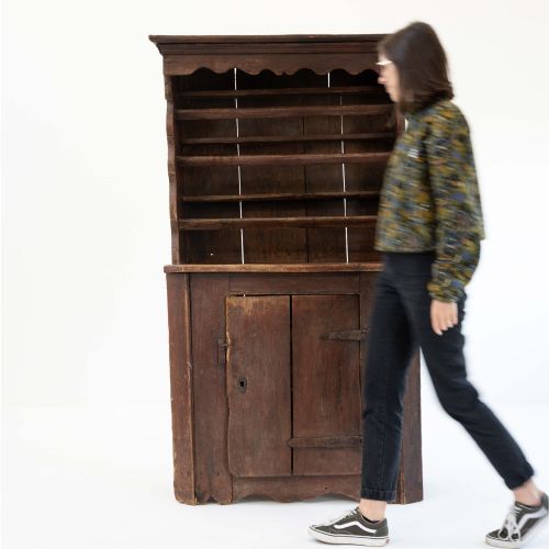 fig 1. A late eighteenth-century dark timber Irish kitchen dresser featuring open plate shelves with scalloped sides above a single-door cupboard base with wrought iron hinges.