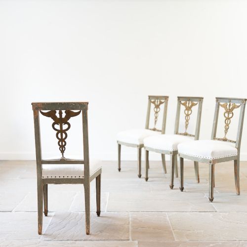 fig 2. A set of four 19th-century Northern European Neoclassical side chairs featuring distressed grey paintwork, off-white linen upholstery, and gilded caduceus motifs in the open back frames.