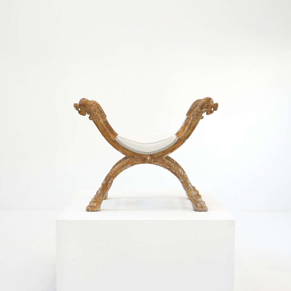 An Italian neoclassical giltwood curule stool with carved lion terminal legs and a pale cream upholstered seat.