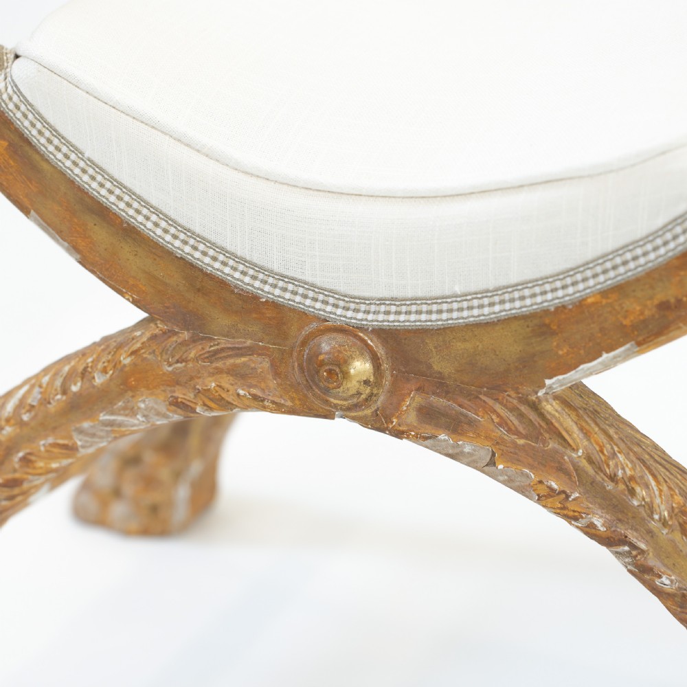 An Italian neoclassical giltwood curule stool with carved lion terminal legs and a pale cream upholstered seat. View VI