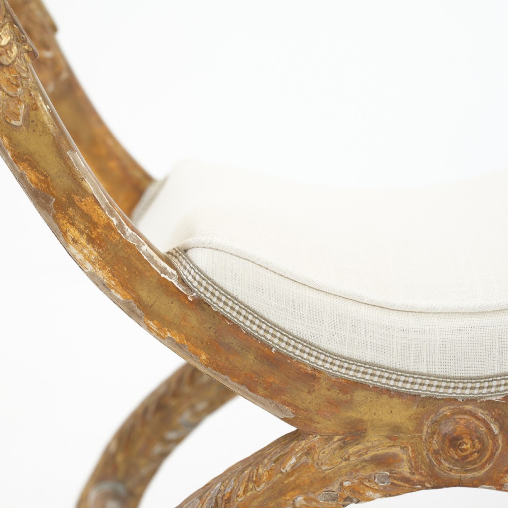 An Italian neoclassical giltwood curule stool with carved lion terminal legs and a pale cream upholstered seat. View VII