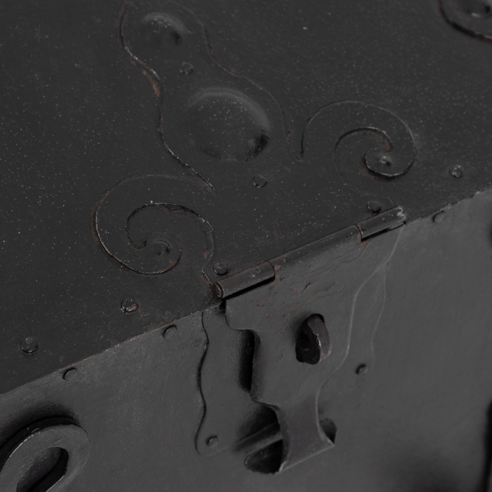 A heavy black wrought iron chest featuring a gabled hinged lid, decorative strap hinges, rivets, and stylised scrollwork appliques. View II