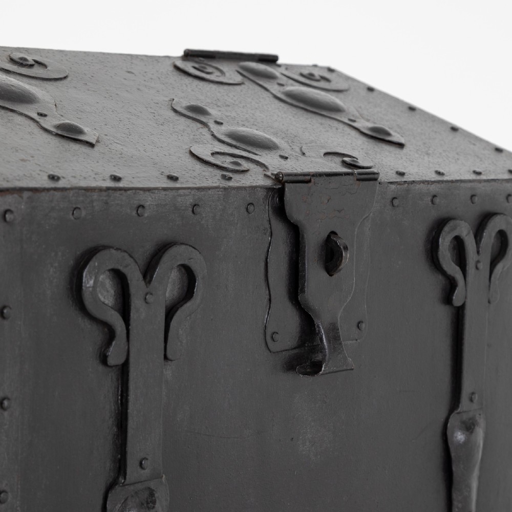 A heavy black wrought iron chest featuring a gabled hinged lid, decorative strap hinges, rivets, and stylised scrollwork appliques. View III
