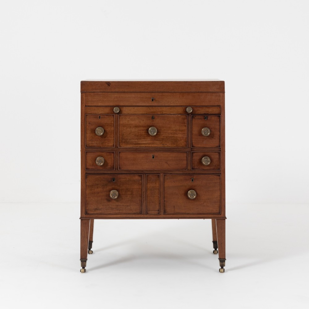A George III mahogany travelling dressing chest featuring multiple drawer arrangements with circular brass handles, raised on square tapered legs with castors.