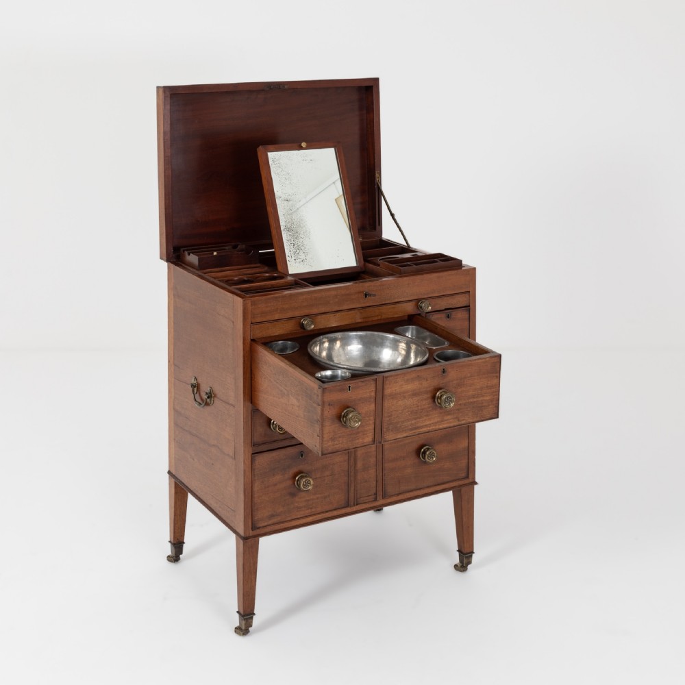 A George III mahogany travelling dressing chest featuring multiple drawer arrangements with circular brass handles, raised on square tapered legs with castors. View V