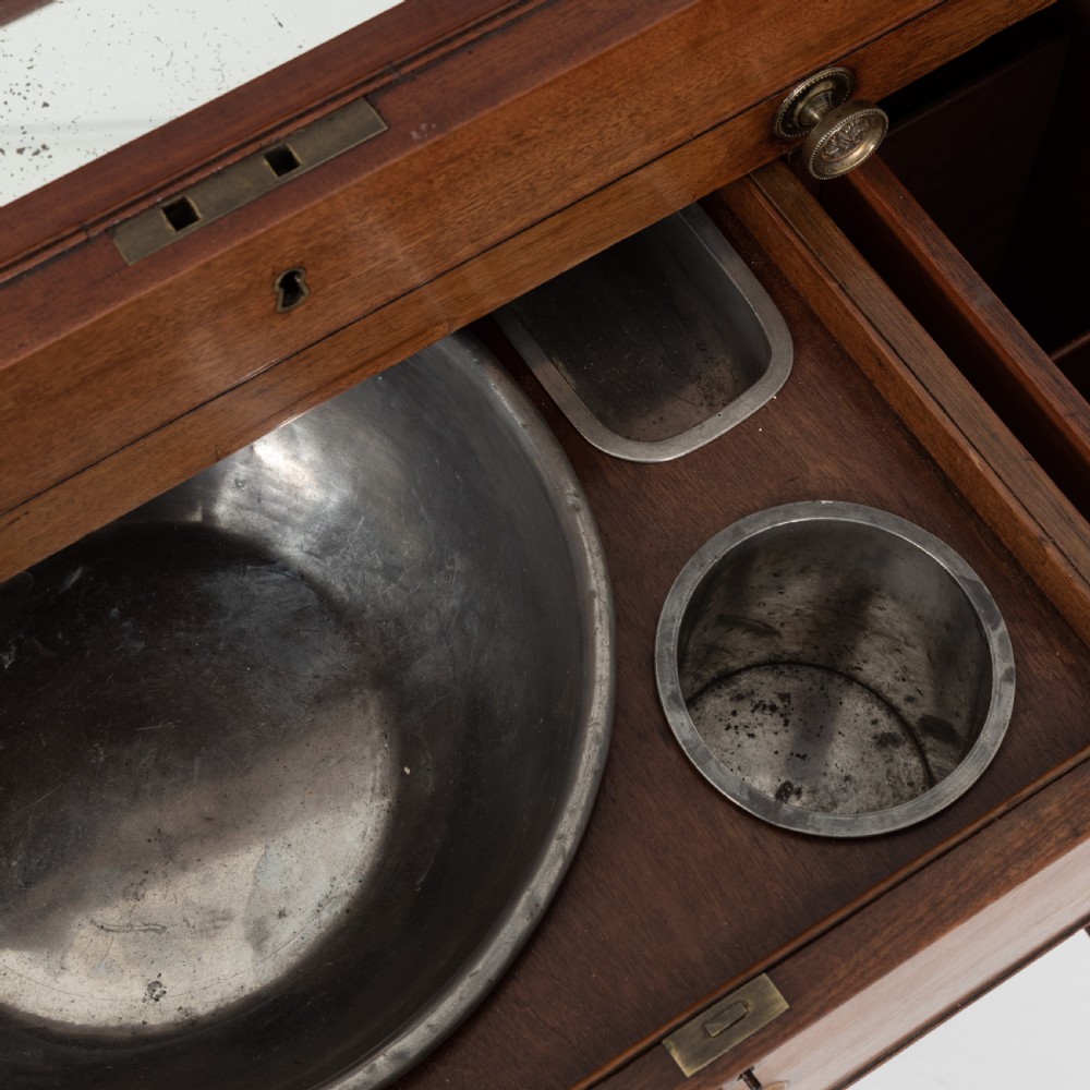 A George III mahogany travelling dressing chest featuring multiple drawer arrangements with circular brass handles, raised on square tapered legs with castors. View XVI