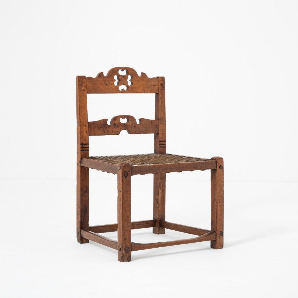 A rustic warm brown hardwood side chair featuring a carved crest rail with a pierced cutout motif and a woven seat.
