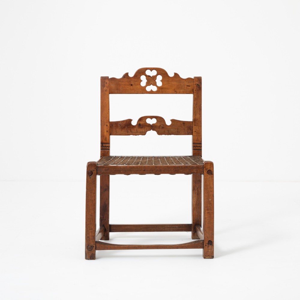 A rustic warm brown hardwood side chair featuring a carved crest rail with a pierced cutout motif and a woven seat. View II