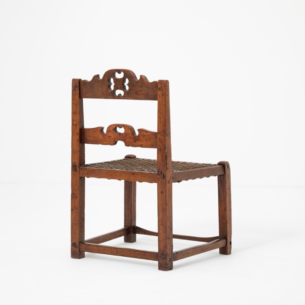 A rustic warm brown hardwood side chair featuring a carved crest rail with a pierced cutout motif and a woven seat. View IV