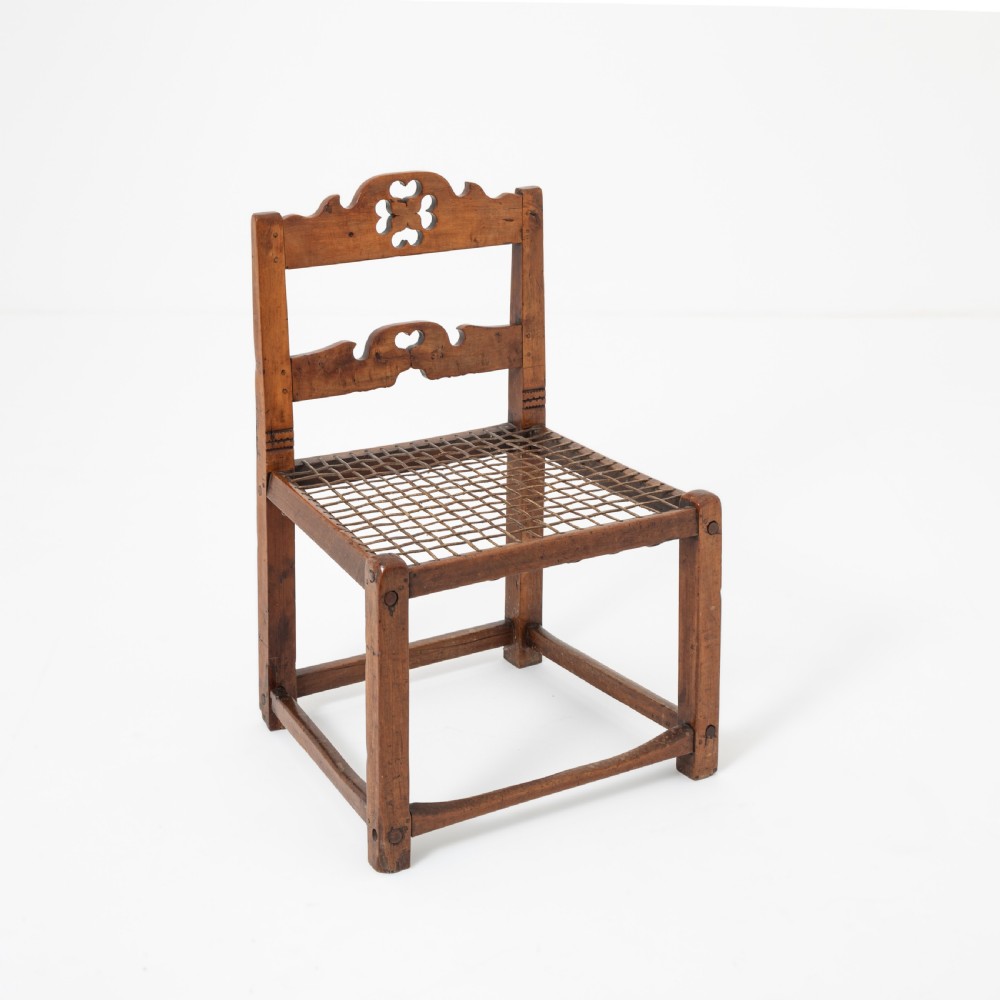 A rustic warm brown hardwood side chair featuring a carved crest rail with a pierced cutout motif and a woven seat. View V