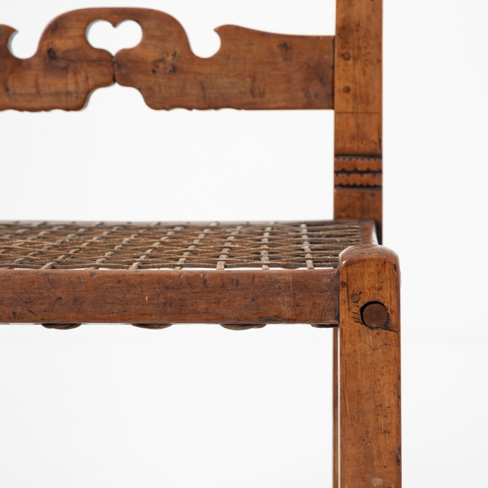 A rustic warm brown hardwood side chair featuring a carved crest rail with a pierced cutout motif and a woven seat. View VI