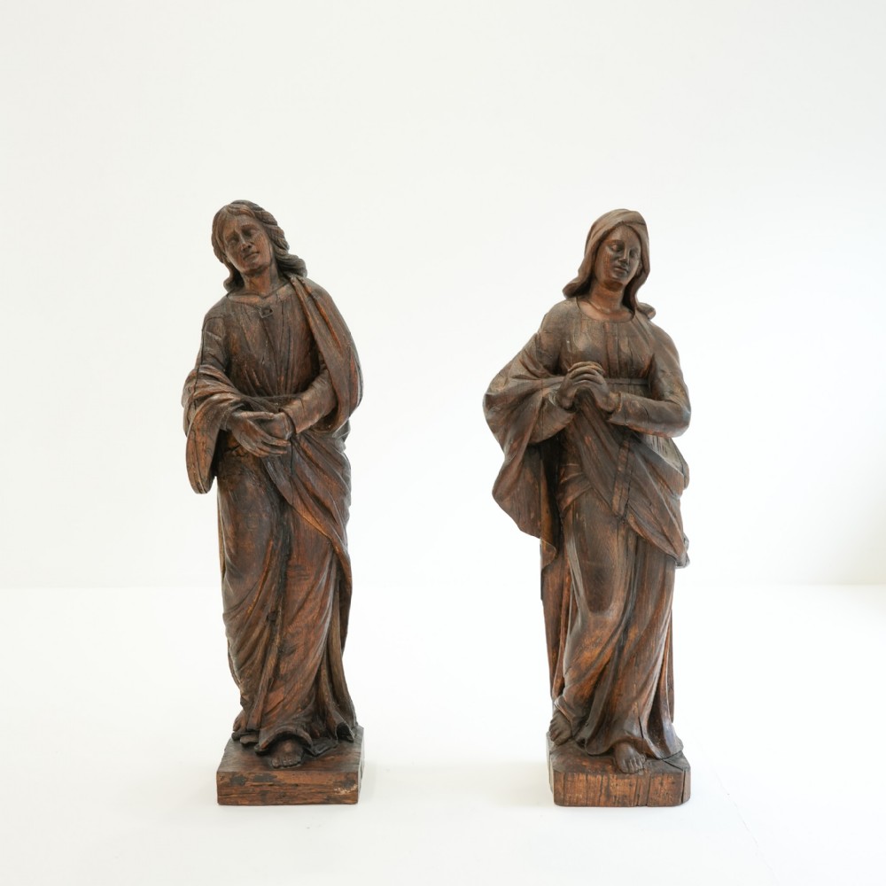 A pair of 18th-century hand-carved dark oak figures depicting robed religious statues standing on integral rectangular wood bases.