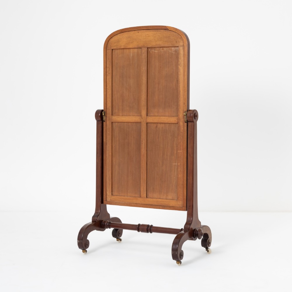A Victorian mahogany cheval mirror featuring an arched rectangular tilting glass plate supported by turned uprights, a low stretcher, and scrolled legs on castors. View II