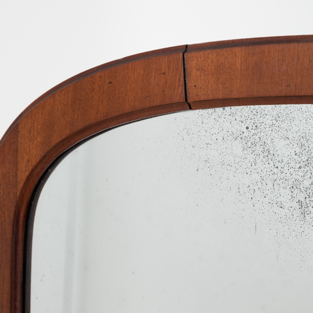 A Victorian mahogany cheval mirror featuring an arched rectangular tilting glass plate supported by turned uprights, a low stretcher, and scrolled legs on castors. View V