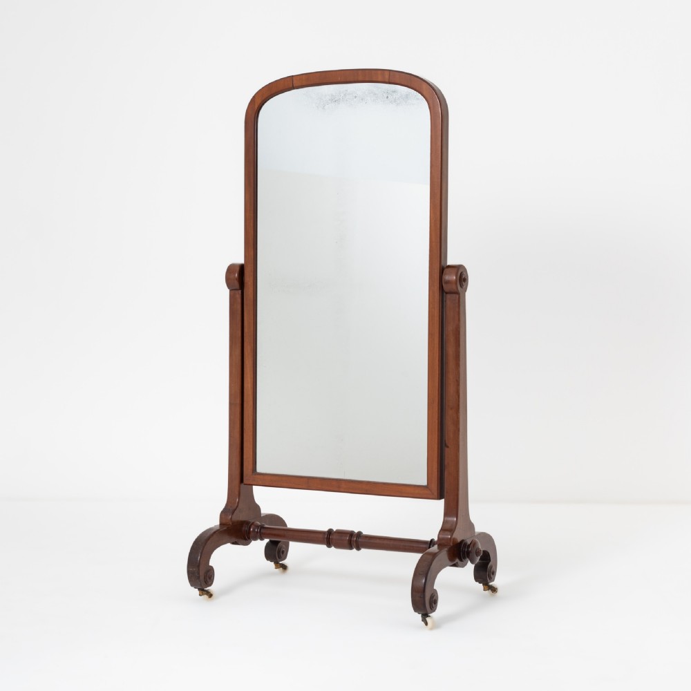 A Victorian mahogany cheval mirror featuring an arched rectangular tilting glass plate supported by turned uprights, a low stretcher, and scrolled legs on castors. View VII