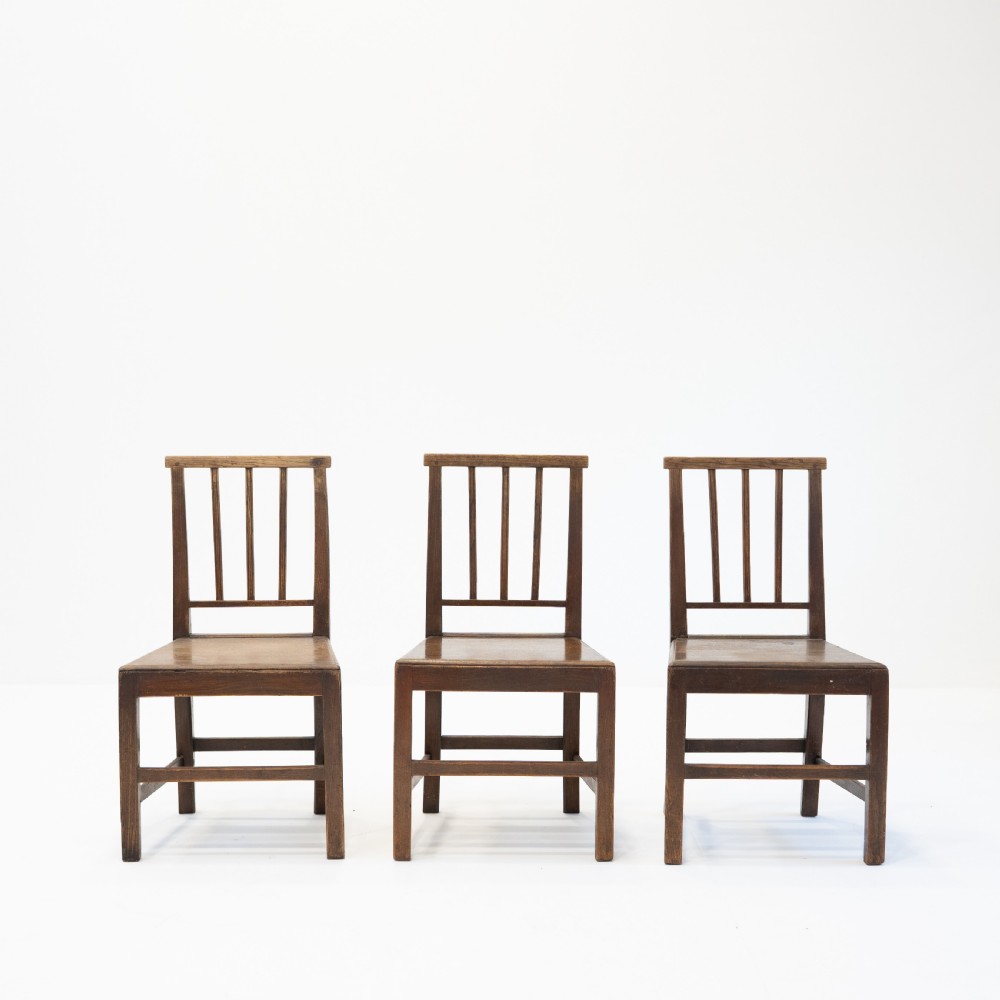 A set of three 18th-century dark wooden farmhouse chairs featuring vertical slat backs, solid wooden seats, and straight legs connected by stretchers. View II