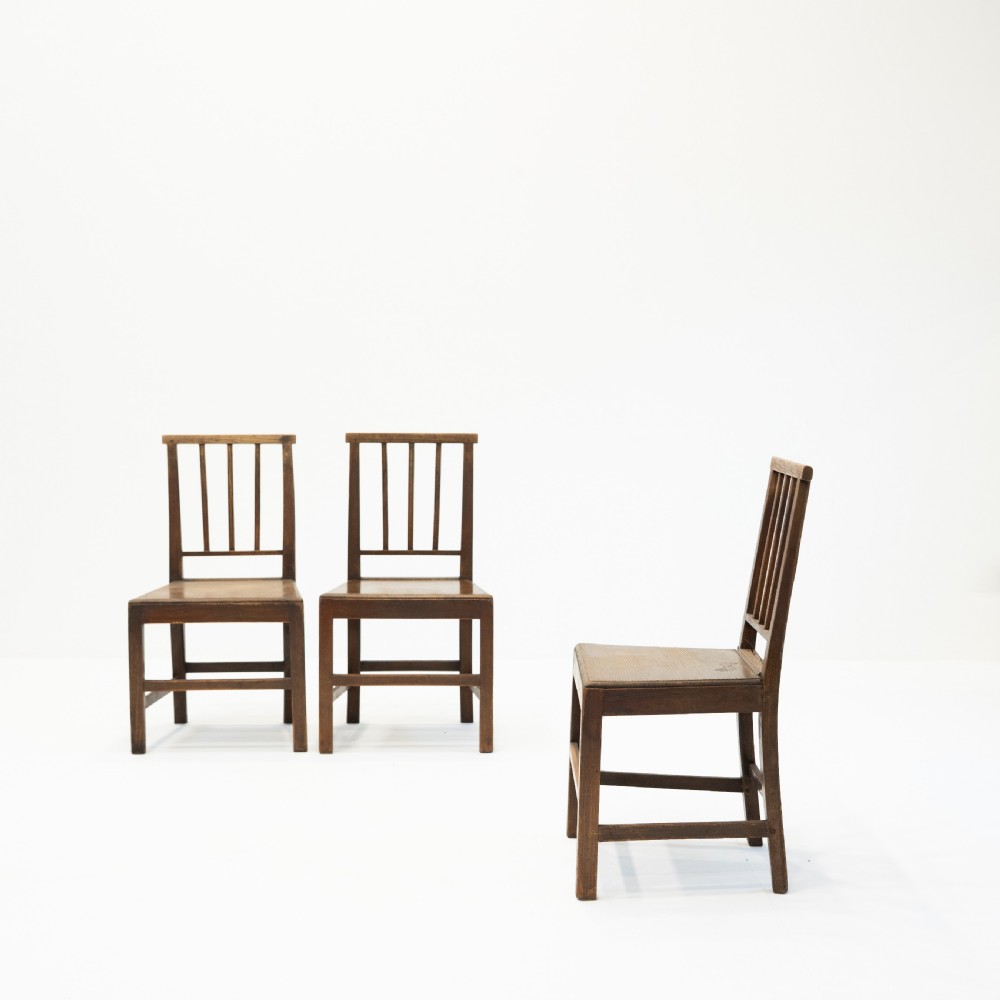 A set of three 18th-century dark wooden farmhouse chairs featuring vertical slat backs, solid wooden seats, and straight legs connected by stretchers. View III