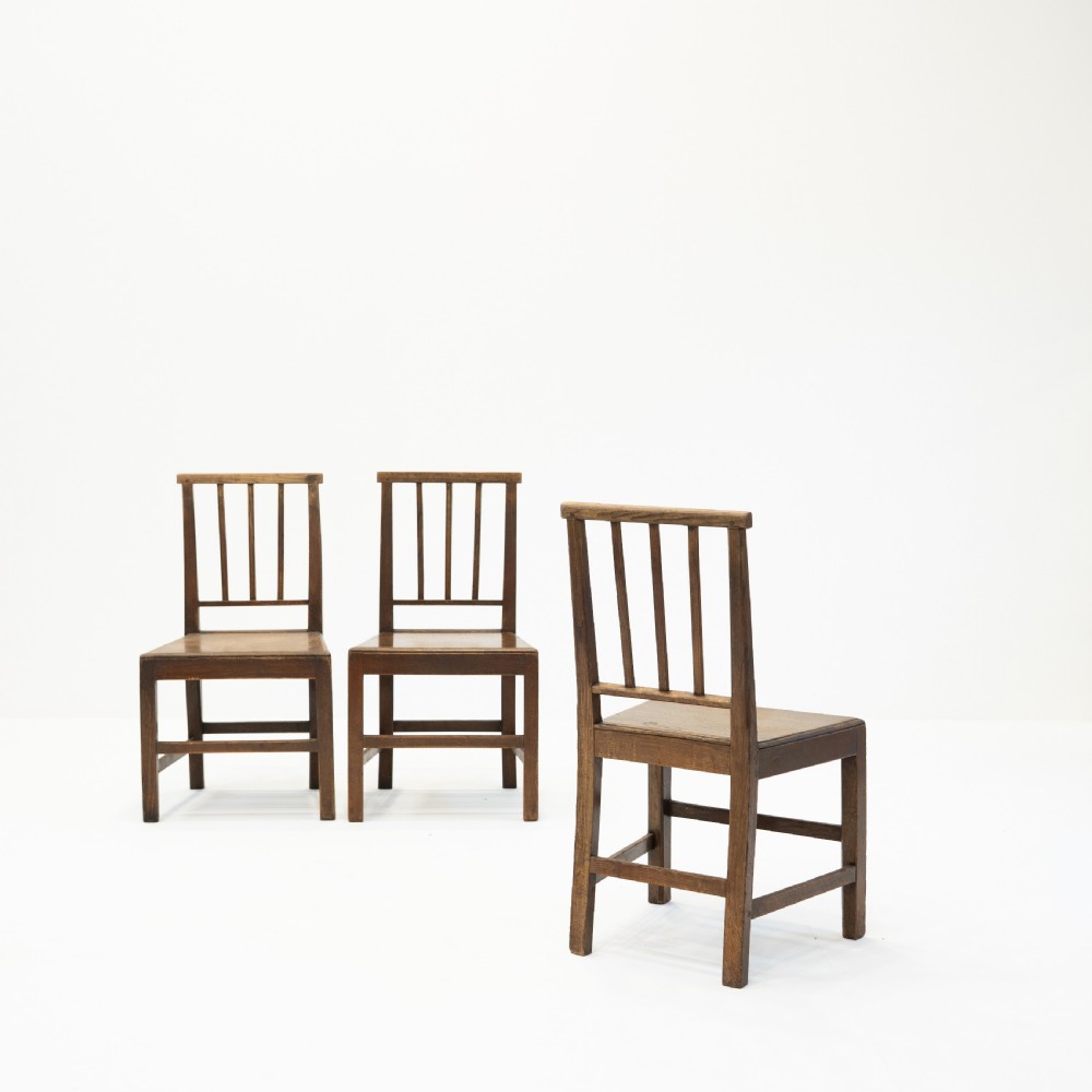 A set of three 18th-century dark wooden farmhouse chairs featuring vertical slat backs, solid wooden seats, and straight legs connected by stretchers. View IV