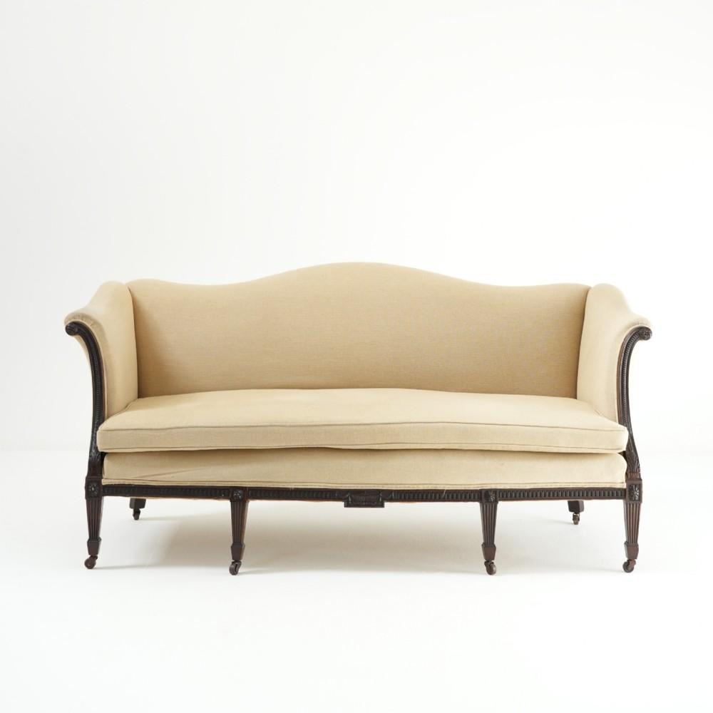 A 19th-century serpentine back sofa upholstered in cream fabric featuring a carved mahogany frame with fluted legs and brass castors.