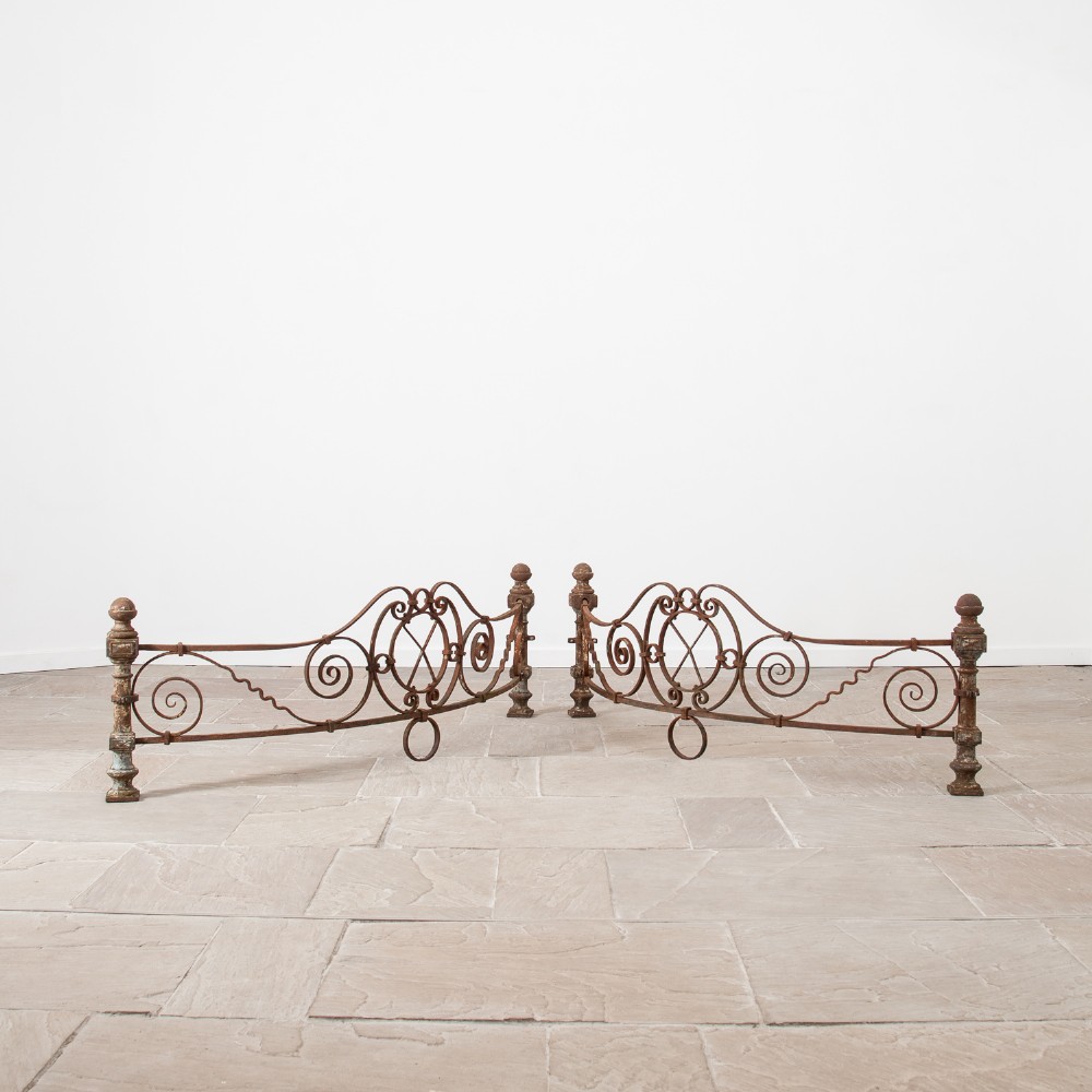 A pair of curved Victorian ironwork railing sections featuring ornate scroll motifs, turned end posts with ball finials, and a heavily rusted surface finish.