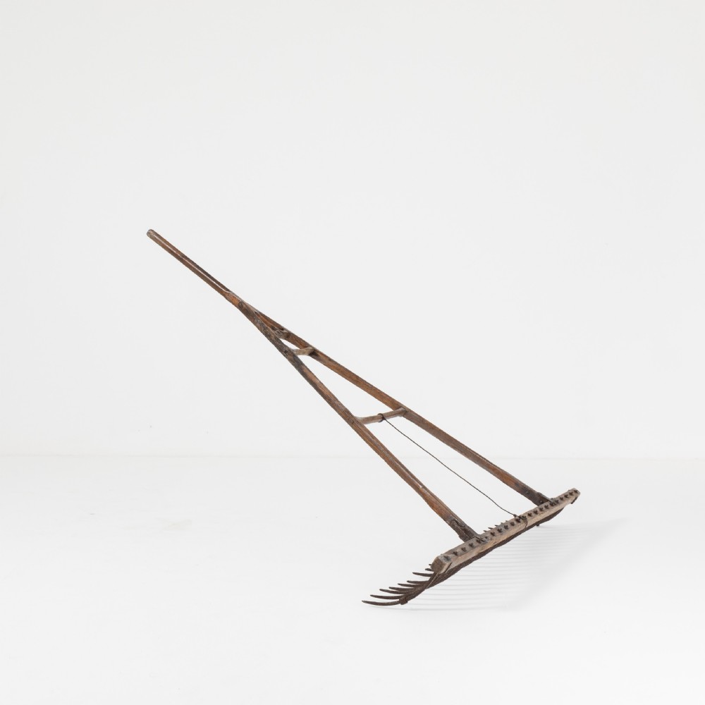 A late nineteenth-century ash hay rake featuring an elongated split-shaft handle and a wide timber head with curved tines. View V