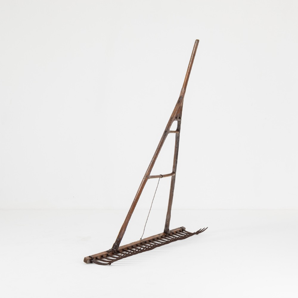 A late nineteenth-century ash hay rake featuring an elongated split-shaft handle and a wide timber head with curved tines. View VI