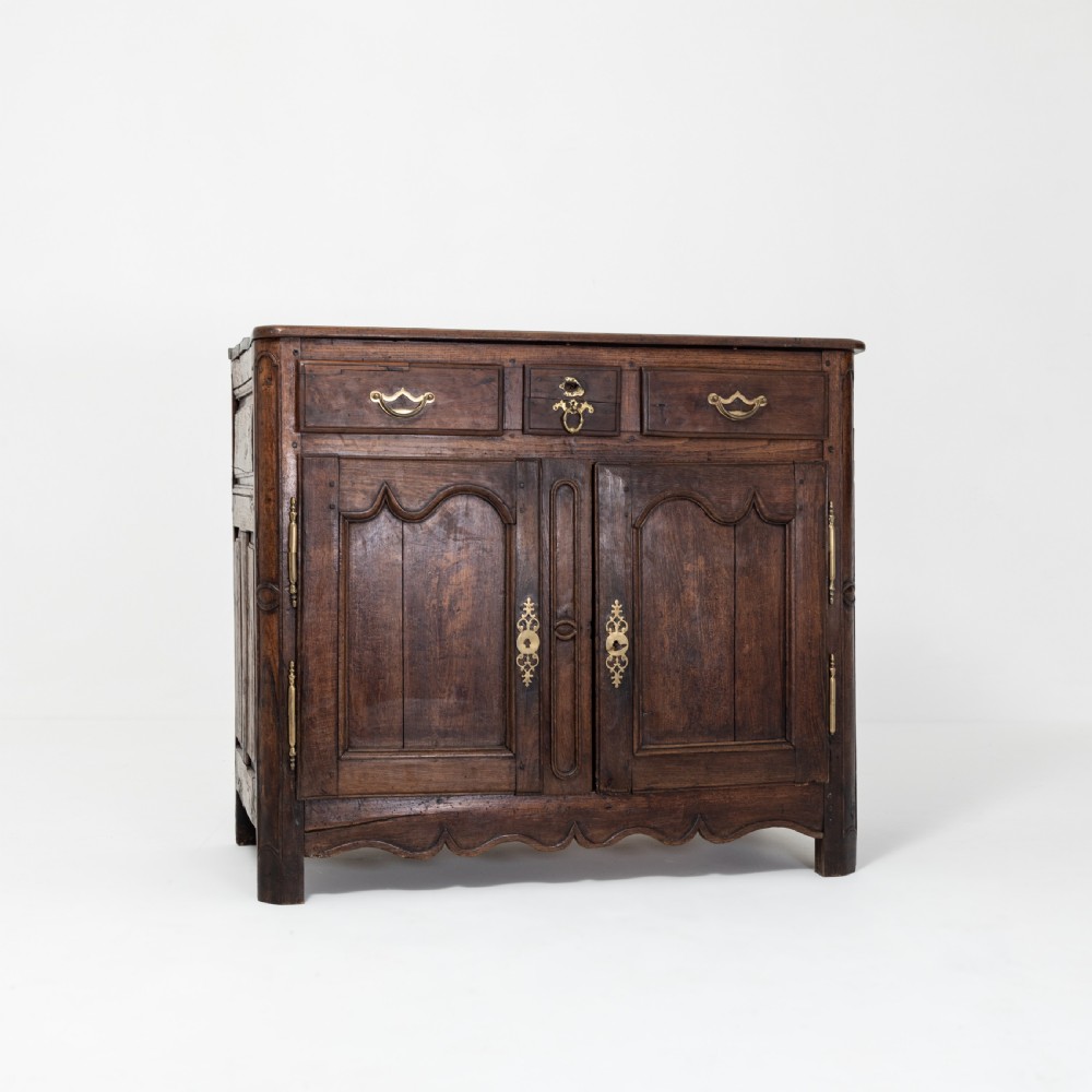 An eighteenth-century Louis XV period dark oak buffet featuring two panelled cabinet doors, three upper drawers, ornate brass hardware, and a shaped apron. View II