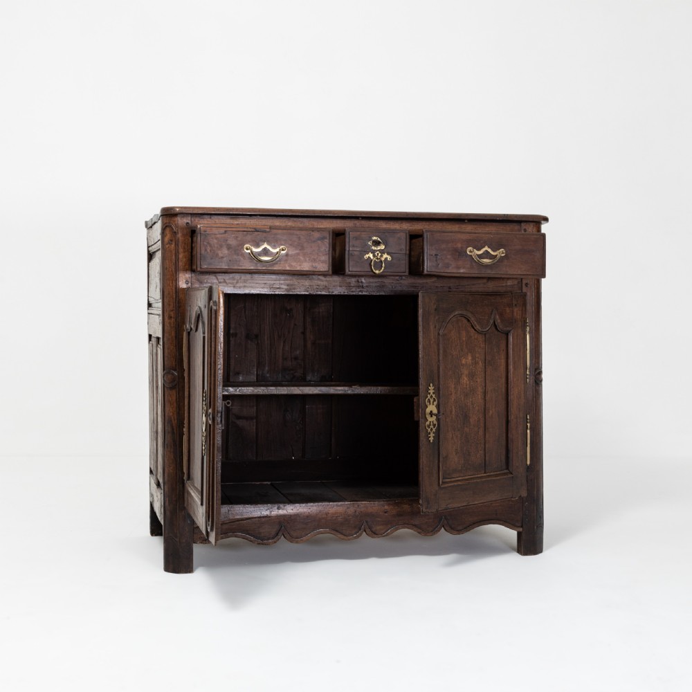 An eighteenth-century Louis XV period dark oak buffet featuring two panelled cabinet doors, three upper drawers, ornate brass hardware, and a shaped apron. View III