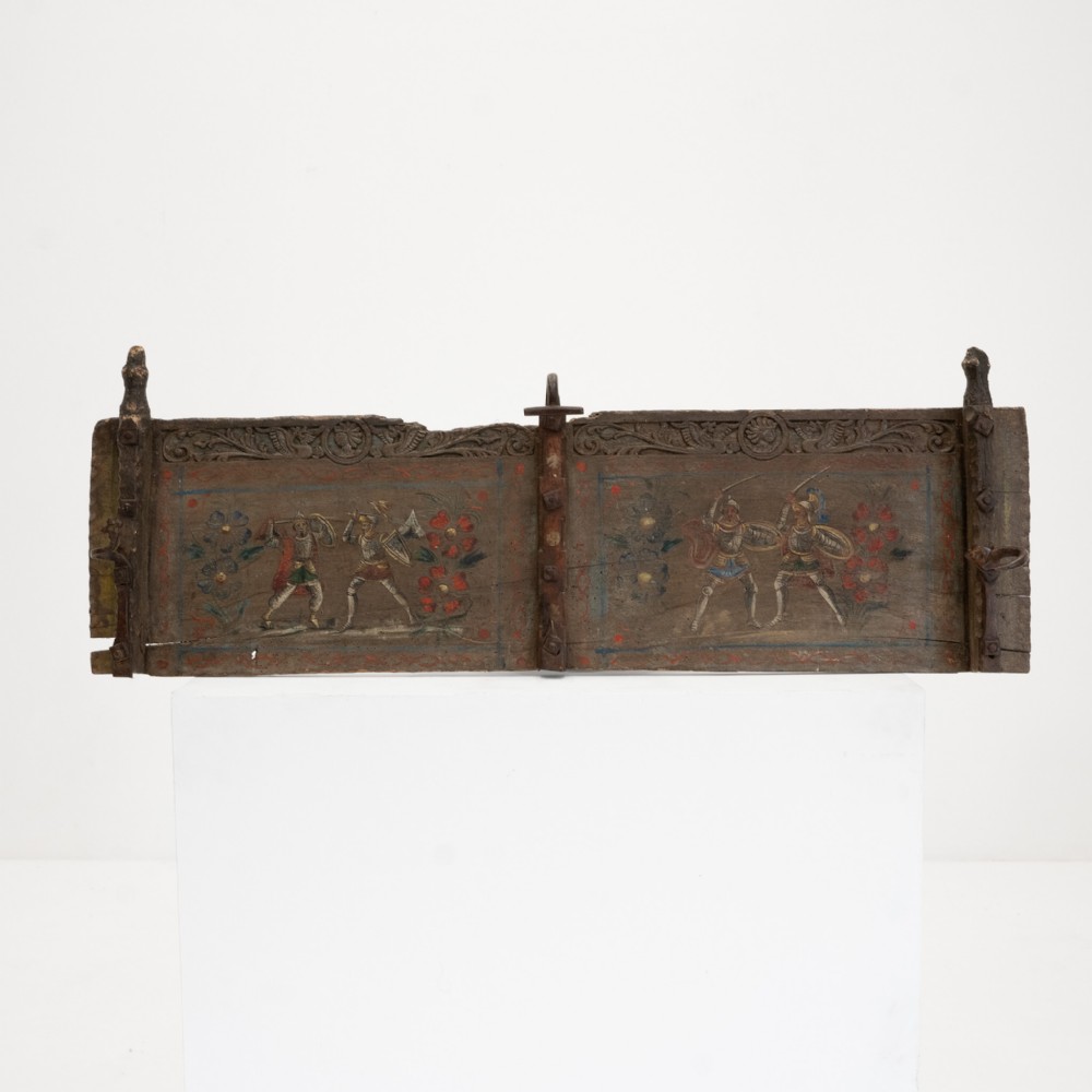 A rectangular dark wood Sicilian cart fragment featuring carved upper borders and hand-painted side panels depicting knights engaged in battle with floral accents.