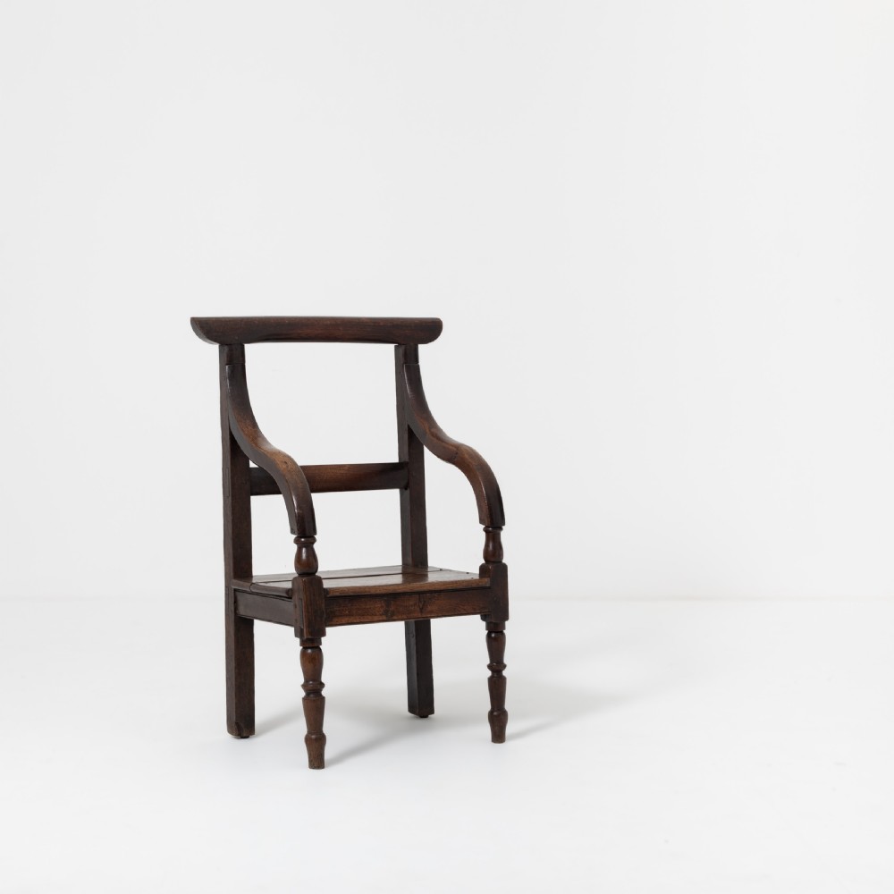 A dark brown 19th-century oak and elm armchair featuring turned front legs, curved arm supports, and a flat top crest rail.