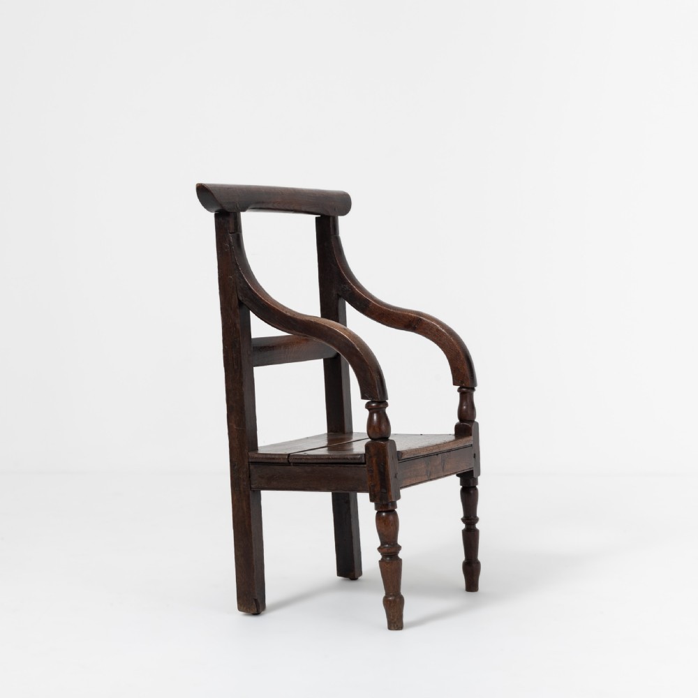 A dark brown 19th-century oak and elm armchair featuring turned front legs, curved arm supports, and a flat top crest rail. View II