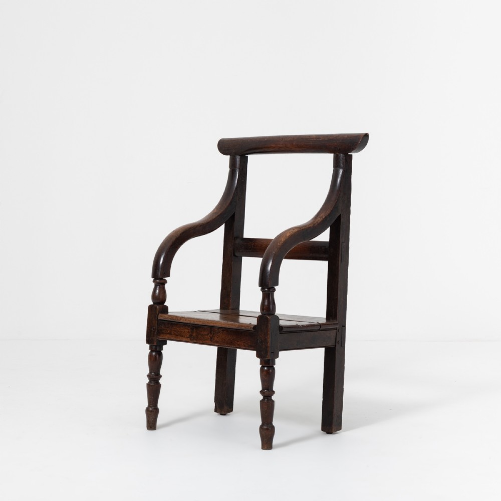 A dark brown 19th-century oak and elm armchair featuring turned front legs, curved arm supports, and a flat top crest rail. View V