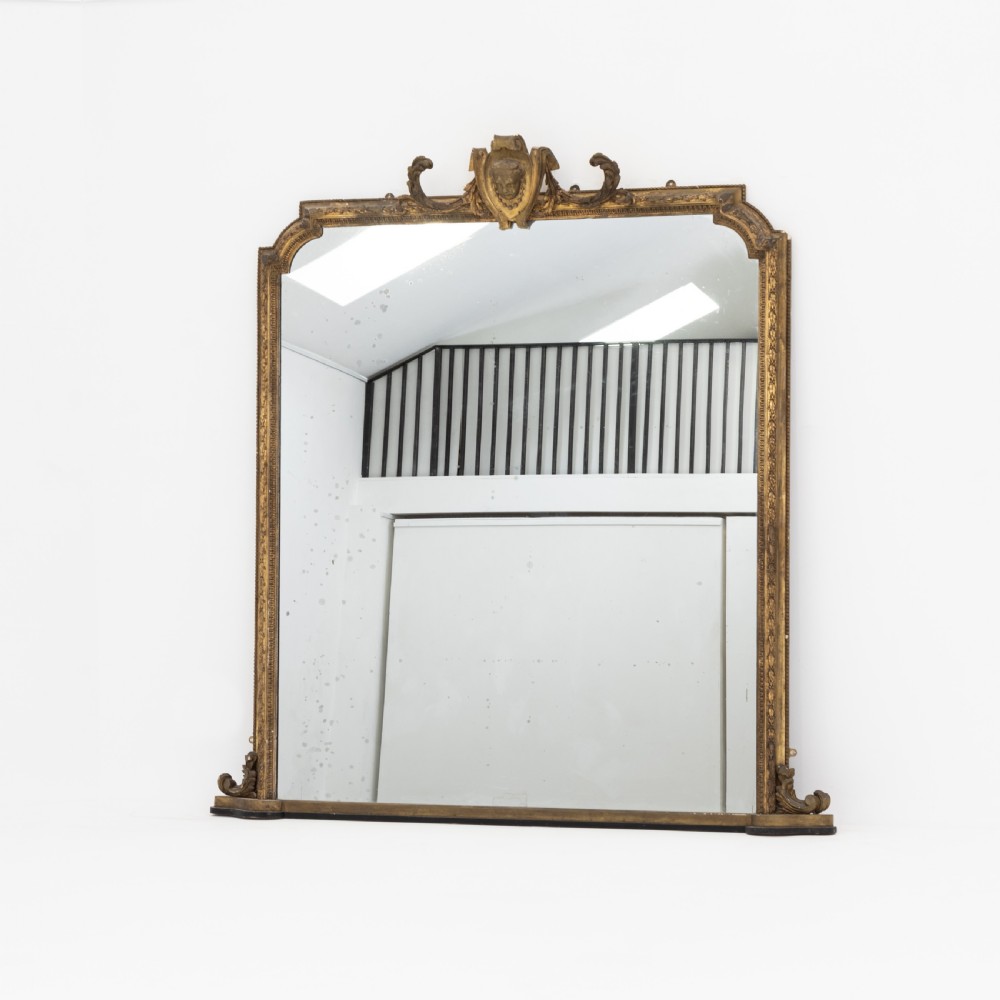 A large Victorian giltwood overmantel mirror featuring an arched frame, detailed cresting with a carved mask, and ornate scroll base feet. View II
