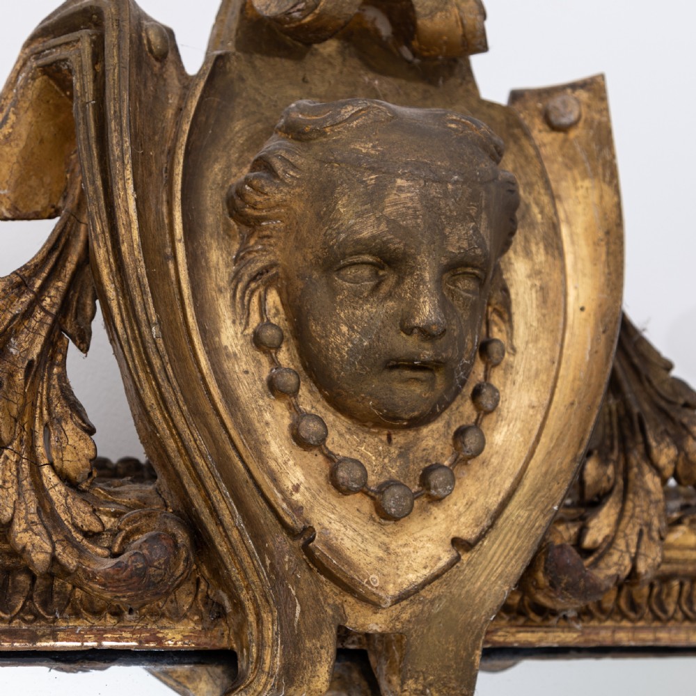 A large Victorian giltwood overmantel mirror featuring an arched frame, detailed cresting with a carved mask, and ornate scroll base feet. View IV