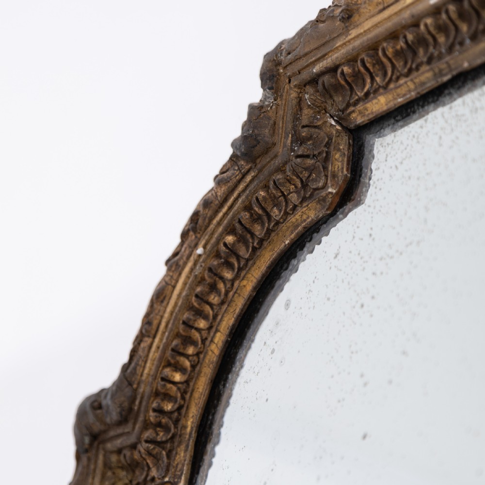 A large Victorian giltwood overmantel mirror featuring an arched frame, detailed cresting with a carved mask, and ornate scroll base feet. View V