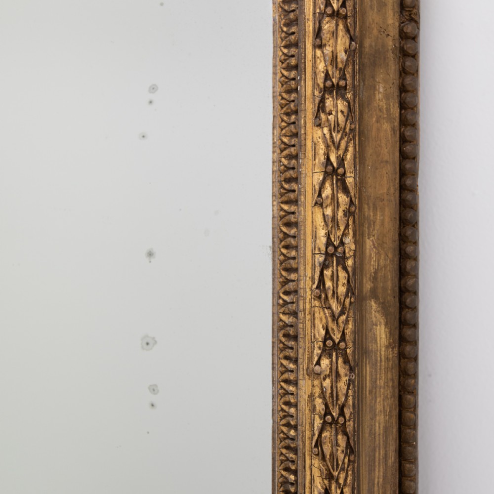 A large Victorian giltwood overmantel mirror featuring an arched frame, detailed cresting with a carved mask, and ornate scroll base feet. View VI