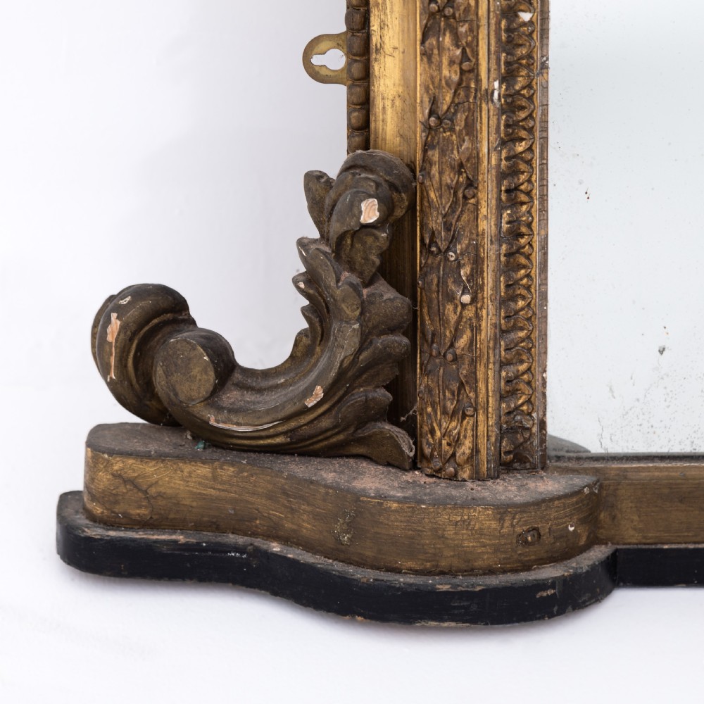 A large Victorian giltwood overmantel mirror featuring an arched frame, detailed cresting with a carved mask, and ornate scroll base feet. View VII