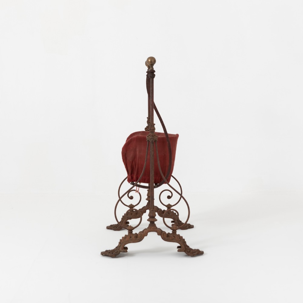 Victorian cast iron freestanding child swing featuring scrolled feet, brass finials, and a red fabric-upholstered suspended seat. View II